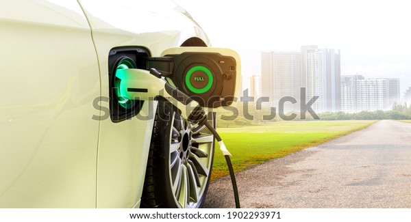 EV Car or Electric car at charging
station with the power cable supply plugged in on Green environment
with a long road leading to the city of the
future.	