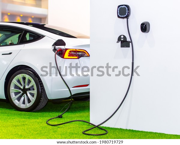 EV Car or Electric car at charging station with\
the power cable supply plugged in. Eco-friendly alternative energy\
concept. Thailand