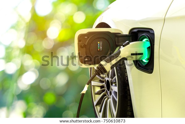 EV Car or\
Electric car at charging station with the power cable supply\
plugged in on blurred nature with soft light background.\
Eco-friendly alternative energy\
concept\
