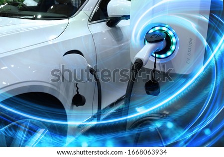 EV Car or Electric vehicle at charging station with the power cable supply plugged in on blurred nature with blue enegy power effect. Eco-friendly sustainable energy concept.