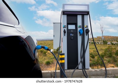 EV car plugged in charger and EV Charger station. Electric car charger station near the highway. Electric car. Zero emission car charging. Carbon free