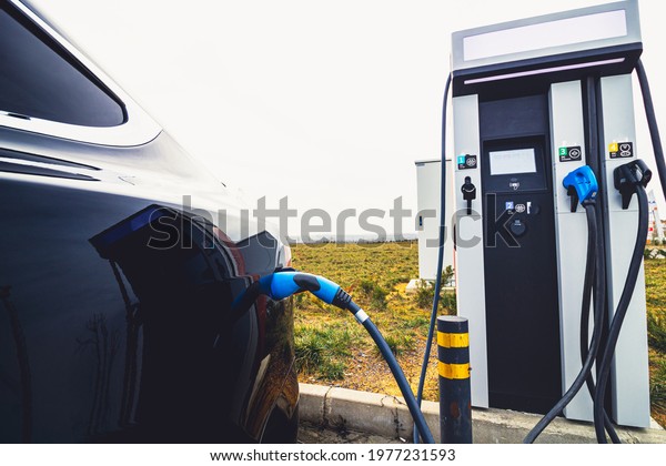 EV car plugged in charger and EV Charger\
station. Electric car charger station near the highway. Electric\
car. Zero emission car charging. Carbon\
free