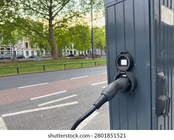 EV charging plug connected to a streetside station by a leafy park in Rotterdam, Netherlands, closeup view.