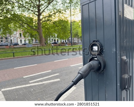 EV charging plug connected to a streetside station by a leafy park in Rotterdam, Netherlands, closeup view.