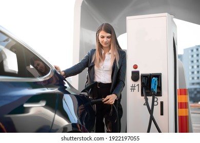 EV charging station, eco fuel concept. Portrait of pretty young girl inserting charging plug into her modern electric car for refueling at city station