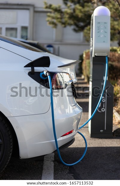 EV electric car pluged charging at a recharge\
station in the city