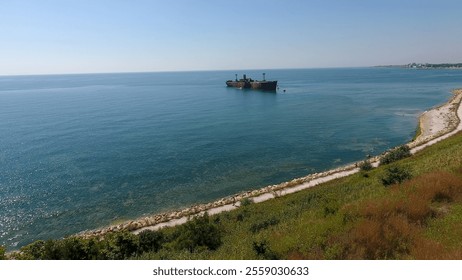 The Evangelia shipwreck rests in calm waters near Costinesti, Romania, with a sandy beach, lush greenery, and a distant view of the town under a clear sky. - Powered by Shutterstock