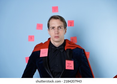 Even Superheroes Experience Professional Burnout. A Man In The Image Of A Hero In A Business Suit And A Red Cape. Tired Of The Continuous Flow Of Tasks.