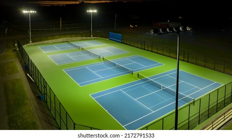 Evening aerial photo of outdoor blue tennis courts with pickleball lines with lights turned on.	
