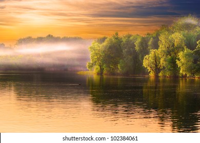 Evening Dnieper river covered with haze. Amazing sunset view, water scape with dramatic yellow sky and beautifully lit trees.