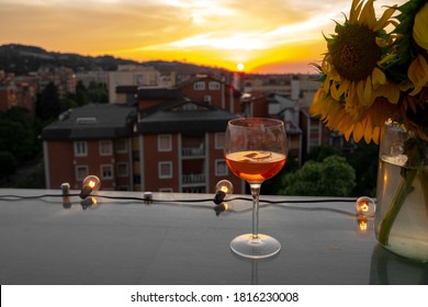 Evening drink in the sunset rooftop bar - Glass of red Aperol Spritz cocktail drink with ice and slice of orange on the rooftop bar. Typical refreshing drink in Italy. Sunset cityscape of Bologna.