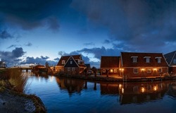 Evening In A Dutch Village By The River. Beautiful Vriver Village In Evening. Evening Lights On River Village Houses. Village River In Evening Time