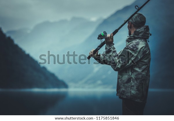 Evening Fly Fishing Time. Caucasian\
Fisherman with Fishing Rod on the Glacial Lake\
Shore.