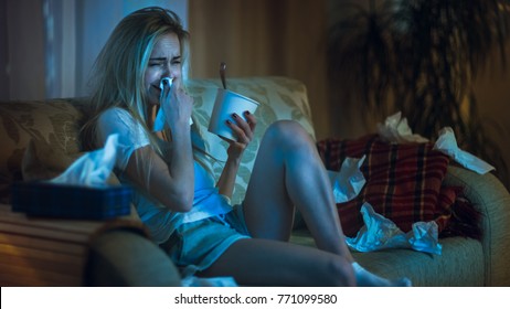 In the Evening Heartbroken Girl Sitting on a Sofa, Crying, Using Tissues, Eating Ice Cream and Watching Drama on TV. Her Room is in Mess. - Shutterstock ID 771099580