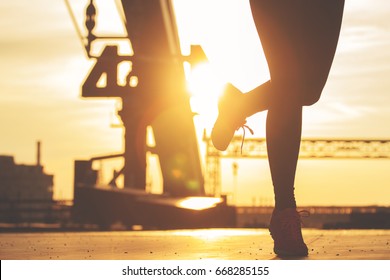 Evening jogging. Closeup silhouette of young sporty woman jogging on the bridge during evening sunset and urban view on background.