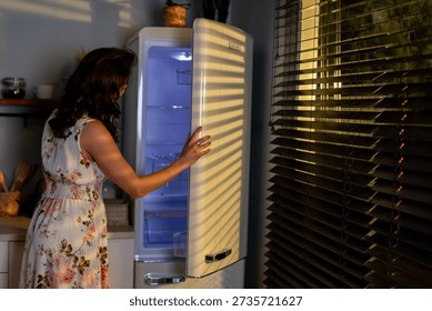 Evening kitchen activity, Lady opens fridge late at night, Woman in floral outfit seeks jar in darkness, Night example of woman retrieving item from cold storage