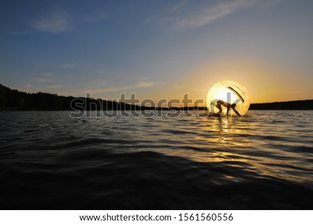 Evening landscape on the river, the sun breaks through the floating zorb in which the person is.