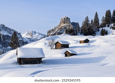 Evening light illuminates wooden cabins in a snow covered valley with the famous Sassongher mountain in the background. The peaceful winter landscape feels almost magical - Powered by Shutterstock