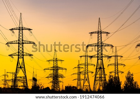 Evening light. Sunset casting red and orange light. Silhouettes of the electric power masts and cables, pylons. Electricity power station.