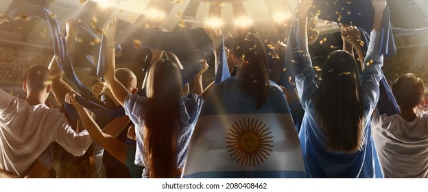 Evening Match. Back View Of Football, Soccer Fans From Argentina Cheering Their Team With Blue-white State Flags And Scarfs At Crowded Stadium. Concept Of Sport, Support, Team Event, Competition