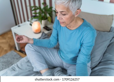 Evening Meditation For A Better Sleep. Mindful Senior Woman Meditating In Lotus Position, Sitting On The Bed At Home