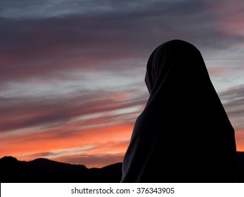 Evening prayers? Muslim woman in chador against sunset sky.