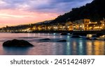 evening or night landscape of evening town coastline in golden lights and sea gulf with calm water and nice reflections with beautisul sunset sky on background