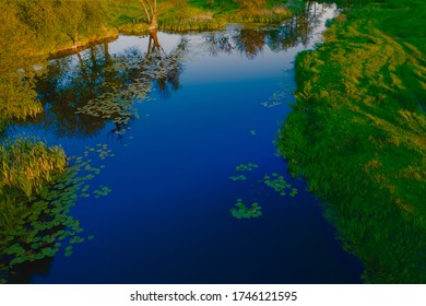 Evening River Landscape. Pure Blue Calm Water Surface Among The Luscious Green Lawn Outside The City. 