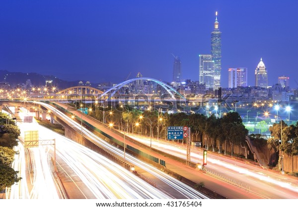 Evening scenery of Taipei City, with Taipei 101\
Tower in XinYi District in downtown area, arch bridges over Keelung\
River & busy car trails on Dike Avenue ~ Prosperous cityscape\
of Taipei at dusk