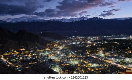 Evening shot of Leh City against snow-capped mountain range at the back and Leh airport on the right. It is blue hour with the sun already set and the city brightens up as they turn on their street