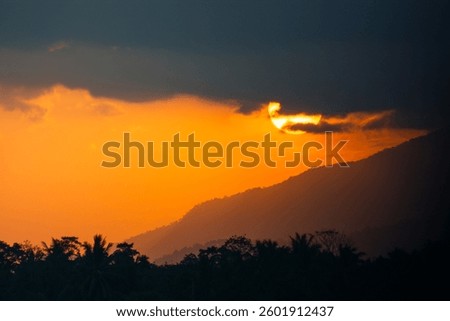 Evening sky, the sun is setting through the mountains, with shadows of trees in front.