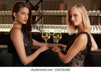 Evening Style. Shot Of Two Women Standing At A Bar In Evening Wear.