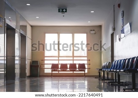 Evening sunlight shines through the glass windows onto empty chairs with elevators on corridor in rest area at hospital 