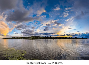 An evening sunset of intermingled cloud patches creates a layered, three-dimensional panoramic picture. The interplay of orange and blue tones blends magically. River reflects colors sky waves.