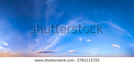 An evening sunset of intermingled cloud patches creates a layered, three-dimensional panoramic picture. The interplay of orange and blue tones blends magically with the setting and shadow. The river reflects the colors of the sky in its waves.