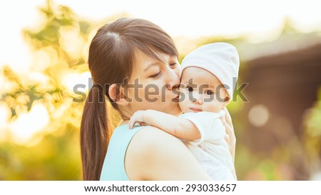 At the evening time before the sunset, 4 months baby feeling happy and smiles with her mother in the garden. Family portrait of Asian family.