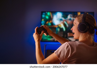 Evening Time, Rest, Day Off. Young Woman Shooter Plays Video Games. Reacts Very Emotionally. Blue Neon Light. A Woman Is Sitting In A Room In Casual Clothes. Youth Culture.