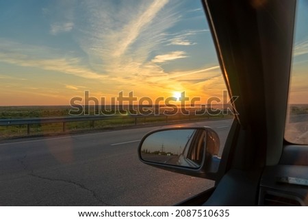 Evening trip to travel on the highway by car at sunset sunrise in the golden hour. Heavenly light.Dramatic evening sky with clouds and rays of the sun view from the window.Panoramic view of clouds