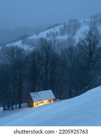 Evening Twilight View Of A Lonely Cabin In A Snowy Mountain Forest In Winter