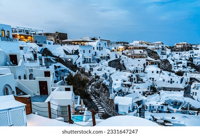 An evening view from afar of hotels, restuarants, and houses on the top of a mountain of the Oia village in Santorini island - Shutterstock ID 2331647247