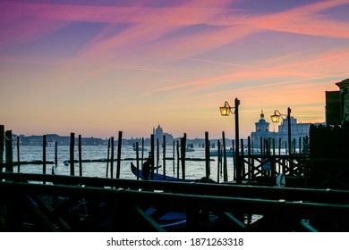 An Evening View Of Gondola Parking Spot: Wooden Columns And Lamps Outlined In Front Of Colorful Night Sky, Contrast Shot Taken From The St Mark's Square (Piazzetta Di San Marco).