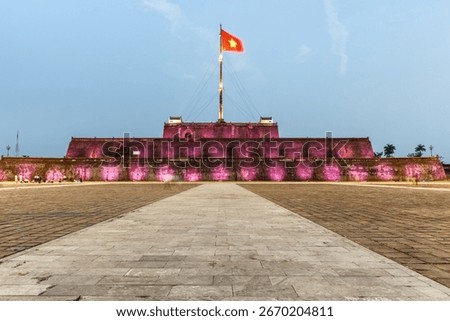 Evening view of a square and the Flag Tower of the Citadel illuminated by pink lights in Hue, Vietnam. Within the Citadel is the Imperial City with the Purple Forbidden City.