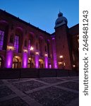 Evening view of Stockholm City Hall beautifully lit in purple. The iconic brick façade, arched windows, and tower create a striking scene under the twilight sky in this historic Swedish landmark.