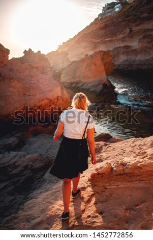 Evening walk of a blonde young girl at a natural sand stone rocks with sunset nature light at the ocean. Punta de El Toro, Mallorca, Spain, Balearics Islands