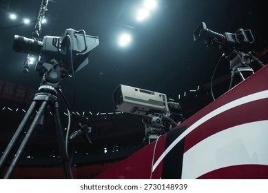 Event broadcasting setup with three professional digital cameras on the tripods. High definition telephoto studio lens. Sport hall lights at the background