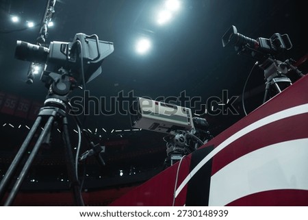 Event broadcasting setup with three professional digital cameras on the tripods. High definition telephoto studio lens. Sport hall lights at the background