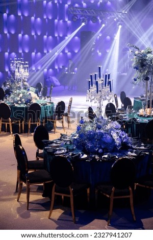 Event decor with chic table setting with blue tablecloths and flowers. Scene in the background. Light filling.