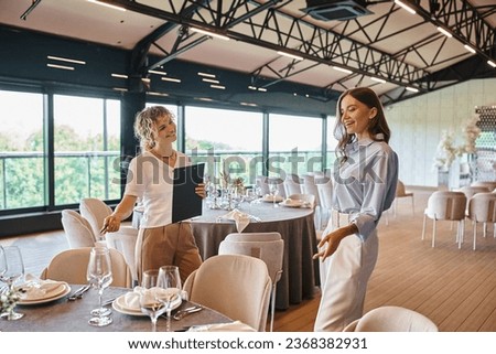 event manager with clipboard showing table with banquet setting to pleased woman in wedding venue