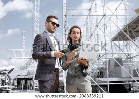 Event managers discuss stage construction. Installation of stage equipment and preparing for a live concert open air. Event manager portrait. Summer music city festival. Teamwork.
