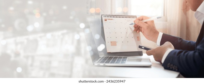 Event planner calendar, agenda, and timetable for 2024. Businessman using his phone to check the planner, making notes on desk calendar at a desk in office. Work planning, event calendar, and calendar - Powered by Shutterstock